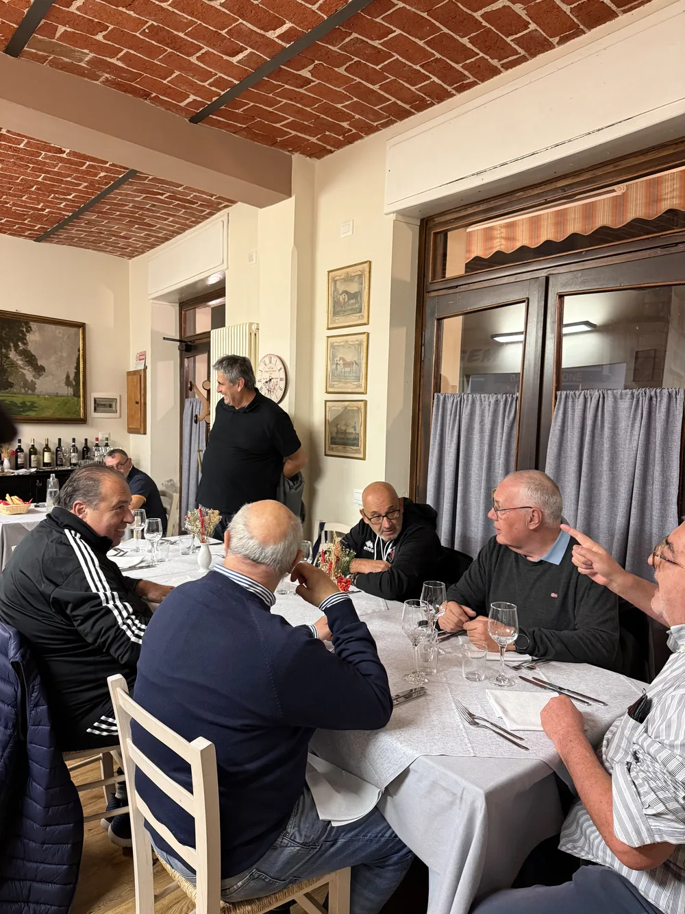 Una tavolata di amici sotto il soffitto in mattoni, accanto alle vetrine sulla strada.