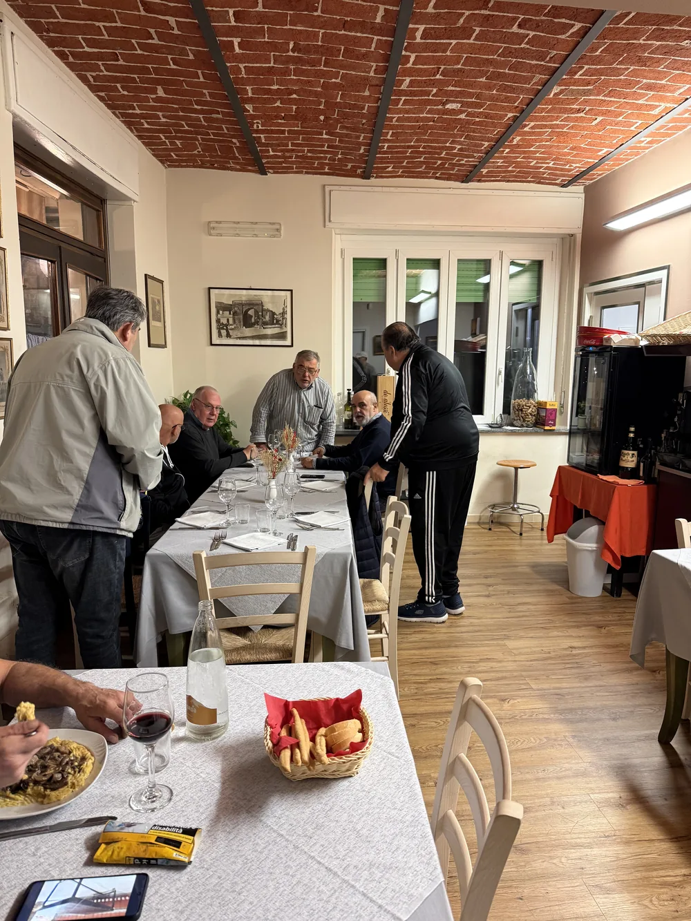 La lunga tavolata apparecchiata nella sala, con i clienti che si salutano prima di cena.